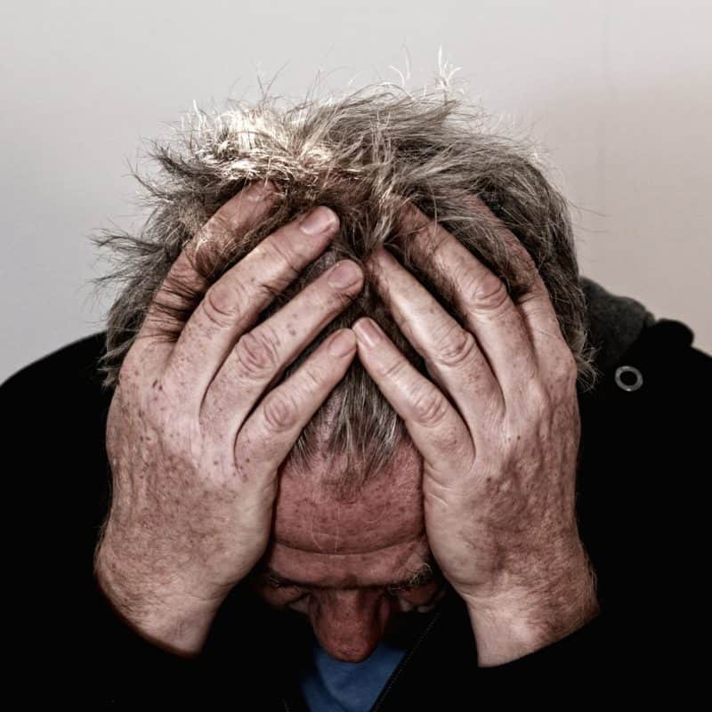 A man holds his hands to his head because he has a migraine headache.