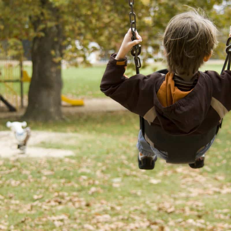 A child on a swing at a playground in autumn for a blog on national childhood injury prevention week