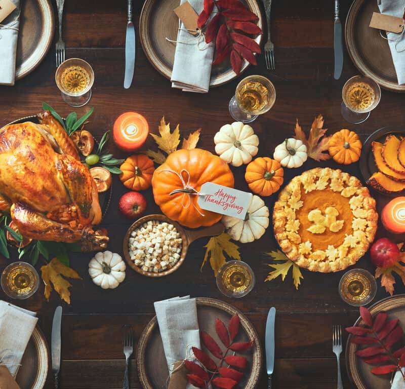 Thanksgiving celebration traditional dinner. Roasted turkey garnished with cranberries on a rustic style table decoraded with pumpkins, vegetables, pie, flowers and candles. Festive table setting