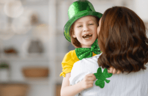 A smiling mom holding her young son, both celebrating St. Patrick's Day with festive shamrock accessories, embodying the spirit of the holiday.