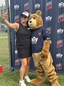 Woman taking a selfie with Ally Medical's mascot, Brave Bear, at a soccer game, both smiling and enjoying the event.