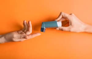 A close-up of an inhaler being passed from one person's hand to another.