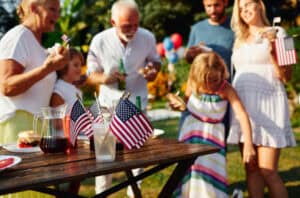 A family enjoying a safe and healthy 4th of July BBQ with children playing and adults grilling in a backyard.