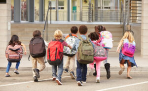 Group of children with backpacks running toward school entrance during back-to-school season.