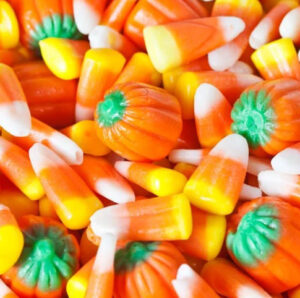 A close-up of colorful Halloween candies, featuring traditional candy corn and pumpkin-shaped treats in vibrant orange, yellow, white, and green colors.